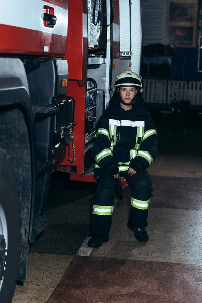 Female firefighter in protective uniform with portable radio set sitting on truck at fire department — Stock Photo