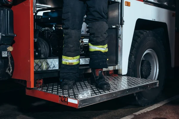 Partial view of firefighter in fireproof uniform standing on truck at fire station — Stock Photo