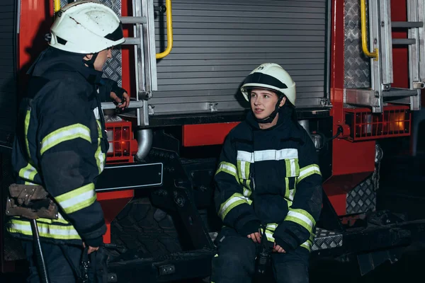 Пожарные в огнеупорной форме и в шлемах беседуют на пожарной станции — стоковое фото