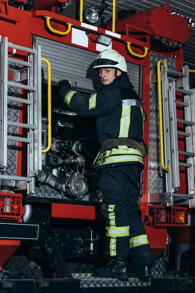 Feuerwehrmann in Schutzuniform und Helm blickt in Feuerwehrhaus auf Kamera — Stockfoto