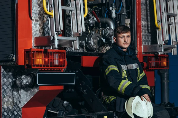 Portrait of male firefighter with protective helmet in hands at truck at fire department — Stock Photo