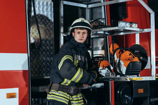 Portrait of firefighter in helmet standing at truck at fire station — Stock Photo