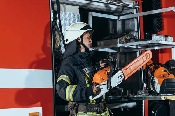 Fireman in helmet holding electric saw while standing at truck at fire station — Stock Photo