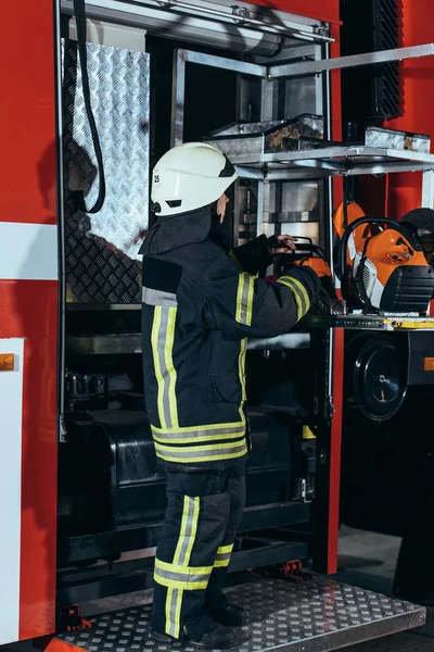 Vista lateral do bombeiro fêmea em pé no equipamento no caminhão no corpo de bombeiros — Fotografia de Stock