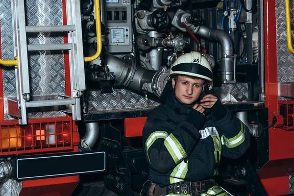 Retrato de bombeiro verificando capacete de proteção no caminhão no quartel de bombeiros — Fotografia de Stock