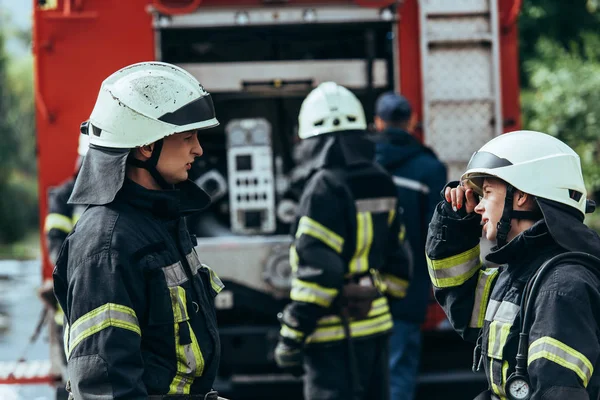 Foco seletivo de bombeiros conversando enquanto brigada em pé no caminhão de bombeiros na rua — Fotografia de Stock