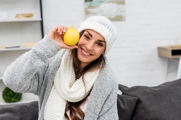 Lächelnde junge Frau in warmer Kleidung mit Zitrone in der Hand und Blick in die Kamera — Stockfoto