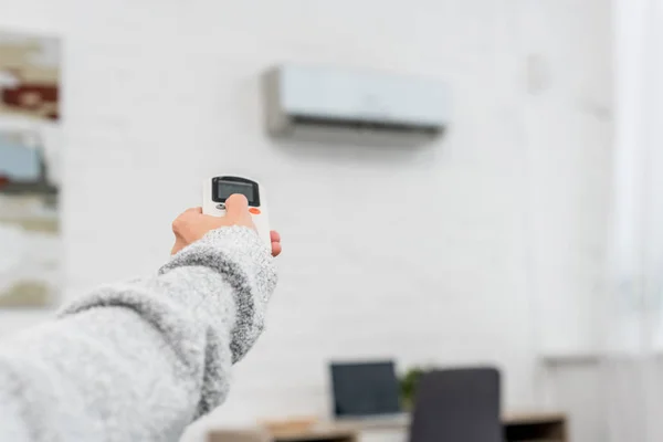 Tiro cortado de mulher em suéter apontando para o ar condicionado com controle remoto — Fotografia de Stock