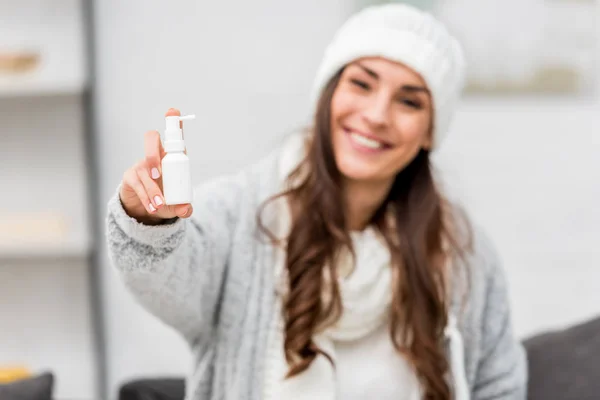 Sick young woman in warm clothes showing nose spray at camera — Stock Photo