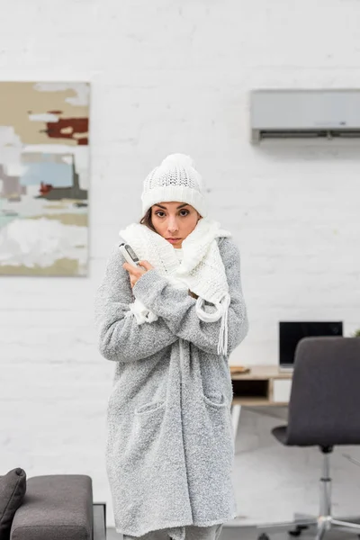 Freezing young woman in warm clothes with air conditioner on background — Stock Photo