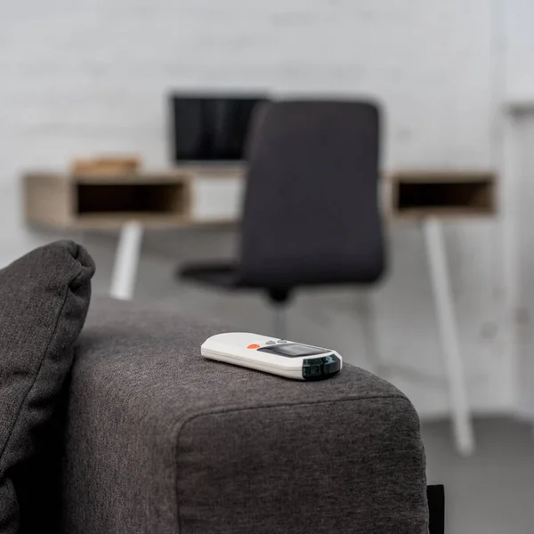 Close-up shot of air conditioner remote control lying on sofa with workplace on background — Stock Photo