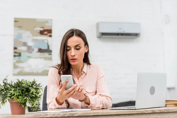 Atractiva joven empresaria usando smartphone mientras trabaja en la oficina - foto de stock