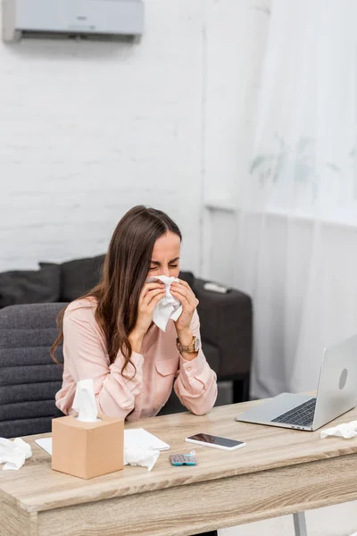 Ill young businesswoman blowing nose with paper napkin at workplace — Stock Photo