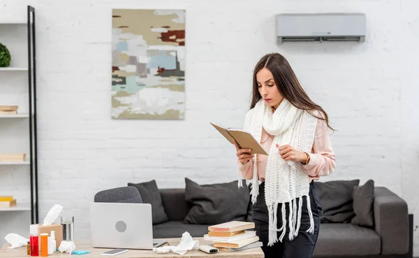 Sick young businesswoman reading book near workplace in office — Stock Photo