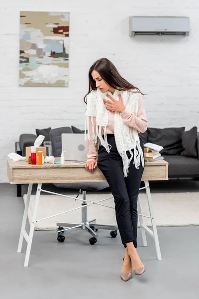 Sick young businesswoman n scarf leaning back at workplace in office — Stock Photo