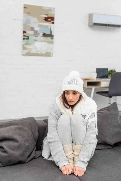 Jeune femme gelée dans des vêtements chauds assis sur le canapé à la maison — Photo de stock