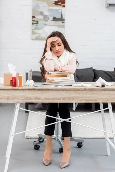 Depressed sick young businesswoman leaning on stack of books at workplace — Stock Photo
