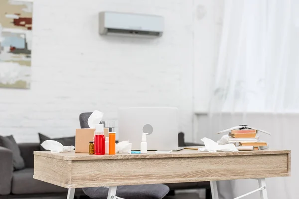 Lieu de travail de bureau désordonné avec ordinateur portable et divers médicaments et serviettes en papier — Photo de stock