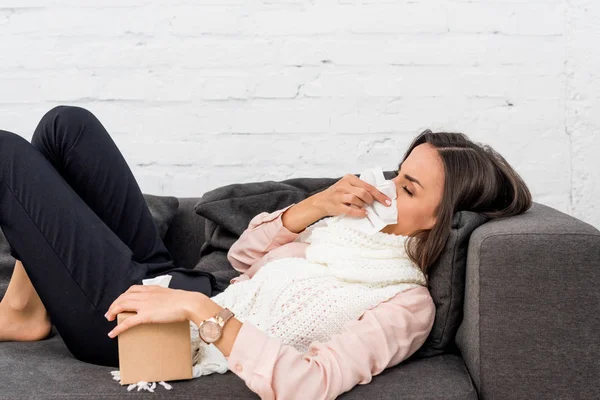 Vue latérale de la jeune femme malade couchée sur le canapé à la maison — Photo de stock