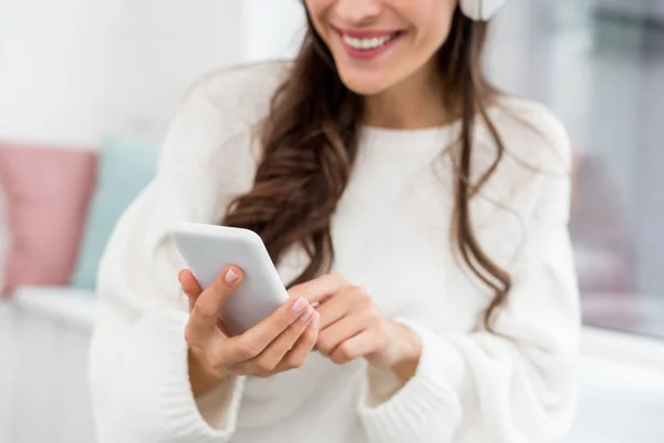 Plan recadré de jeune femme souriante écoutant de la musique avec smartphone et écouteurs sans fil — Photo de stock