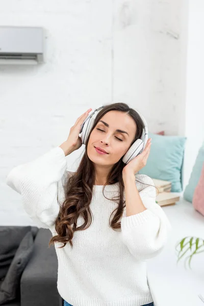 Hermosa mujer joven escuchando música con auriculares inalámbricos en casa - foto de stock
