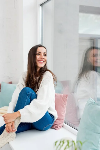 Attractive young woman relaxing on windowsill with cushions and looking up — Stock Photo