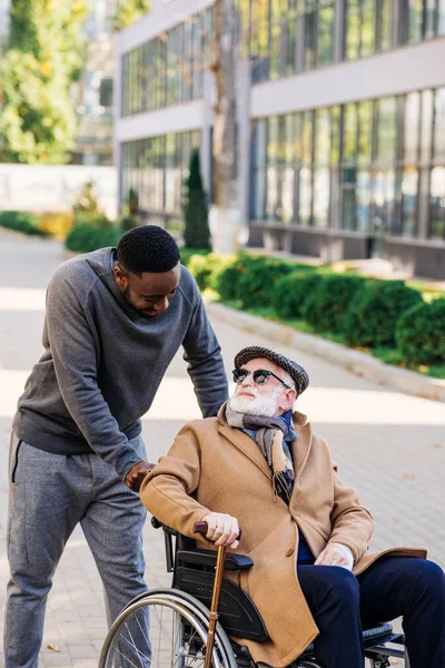 Senior disabled man in wheelchair and african american man talking on street — Stock Photo