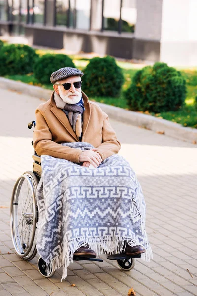 Старший інвалідний чоловік у інвалідному кріслі з пледом на ногах на вулиці — стокове фото