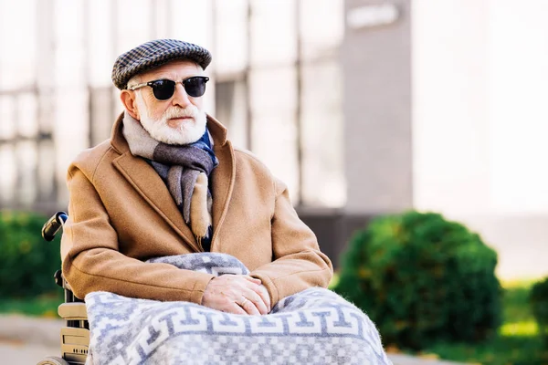 Handsome senior disabled man in wheelchair with plaid on legs on street — Stock Photo