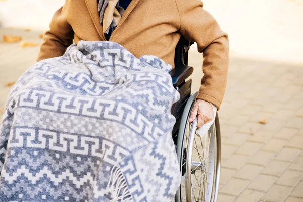 Senior disabled man in wheelchair with plaid on legs riding by street — Stock Photo