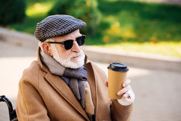 Close-up portrait of senior disabled man in wheelchair holding paper cup of coffee on street — Stock Photo