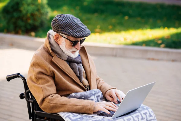 Senior disabled man in wheelchair with plaid using laptop on street — Stock Photo