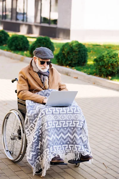 Hombre discapacitado senior concentrado en silla de ruedas usando portátil en la calle - foto de stock