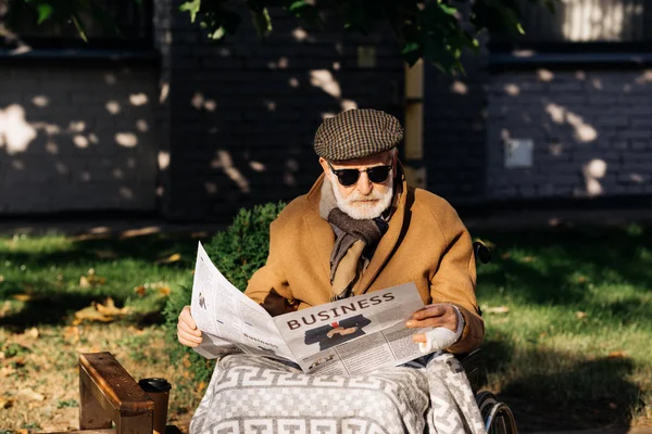 Bonito sênior deficiente homem em cadeira de rodas lendo jornal de negócios na rua — Fotografia de Stock