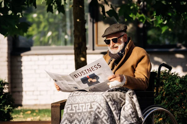 Idoso deficiente em cadeira de rodas lendo jornal de negócios na rua — Fotografia de Stock