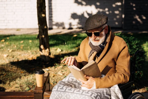 Handsome senior disabled man in wheelchair reading book on street — Stock Photo