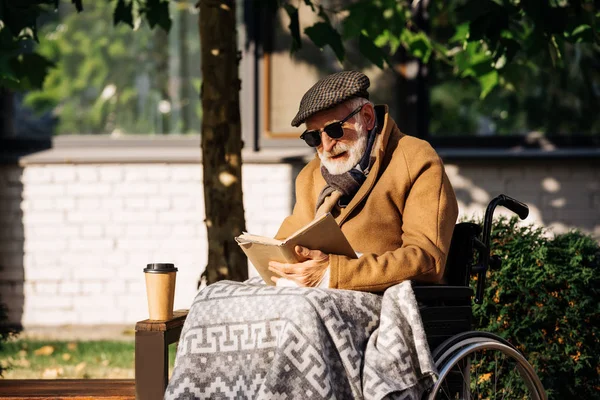 Anciano discapacitado en silla de ruedas con libro de lectura válido en la calle - foto de stock