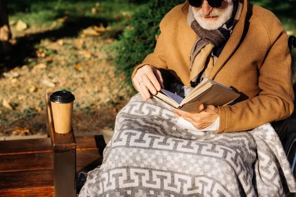 Cropped shot of senior disabled man in wheelchair reading book on street — Stock Photo