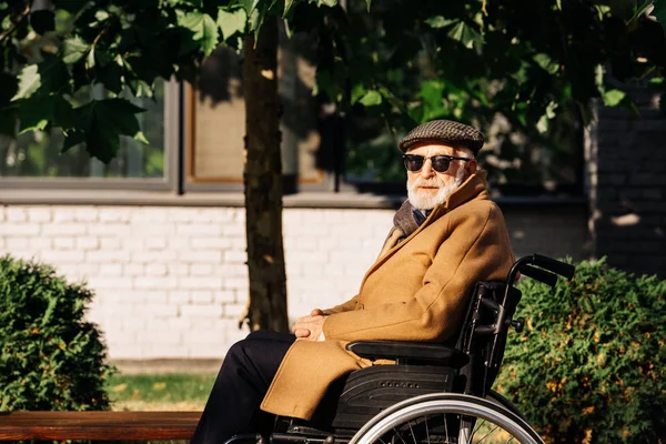 Side view of senior disabled man sitting in wheelchair on street and looking at camera — Stock Photo