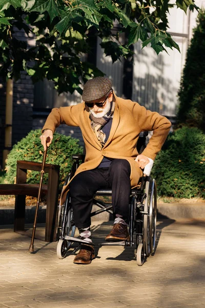 Anziano disabile uomo cercando di alzarsi dalla sedia a rotelle con bastone da passeggio sulla strada — Foto stock