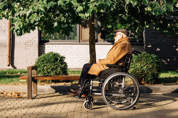 Вид сбоку пожилого инвалида, сидящего в инвалидной коляске на улице — стоковое фото