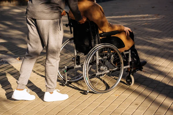 Cropped shot of disabled man in wheelchair and nurse riding on street — Stock Photo