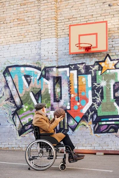 Ativo idoso deficiente homem em cadeira de rodas jogando basquete na rua — Fotografia de Stock