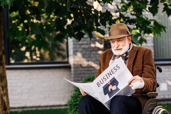 Senior disabled man in wheelchair reading business newspaper on street — Stock Photo