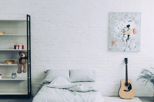 Hochwinkelblick auf modernes Schlafzimmer mit Regalen, Gitarre und Malerei an weißer Ziegelwand — Stockfoto