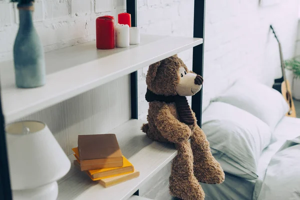 Vue grand angle de l'ours en peluche assis sur des étagères avec des livres et des bougies à la maison — Photo de stock