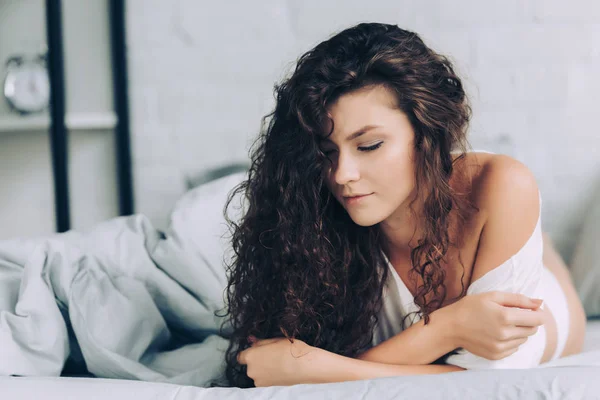 Selective focus of curly young woman laying in bed during morning time at home — Stock Photo