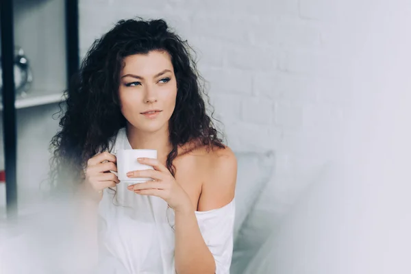 Selective focus of curly woman drinking coffee in bed during morning time at home — Stock Photo