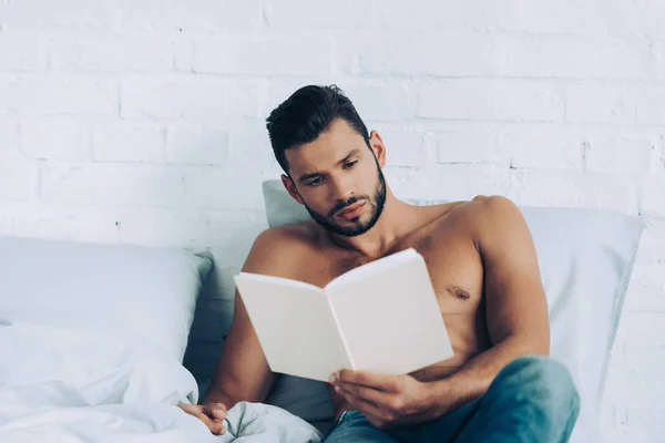Shirtless muscular homem leitura livro durante o horário da manhã no quarto em casa — Fotografia de Stock