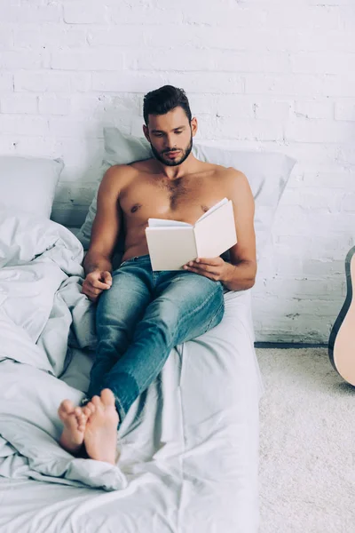 High angle view of shirtless muscular man reading book during morning time in bedroom at home — Stock Photo